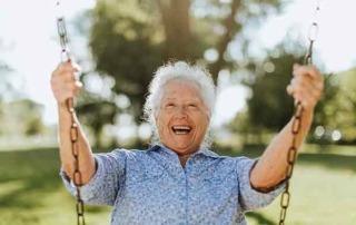 Fröhliche ältere Frau auf einer Schaukel auf einem Spielplatz (116690128)